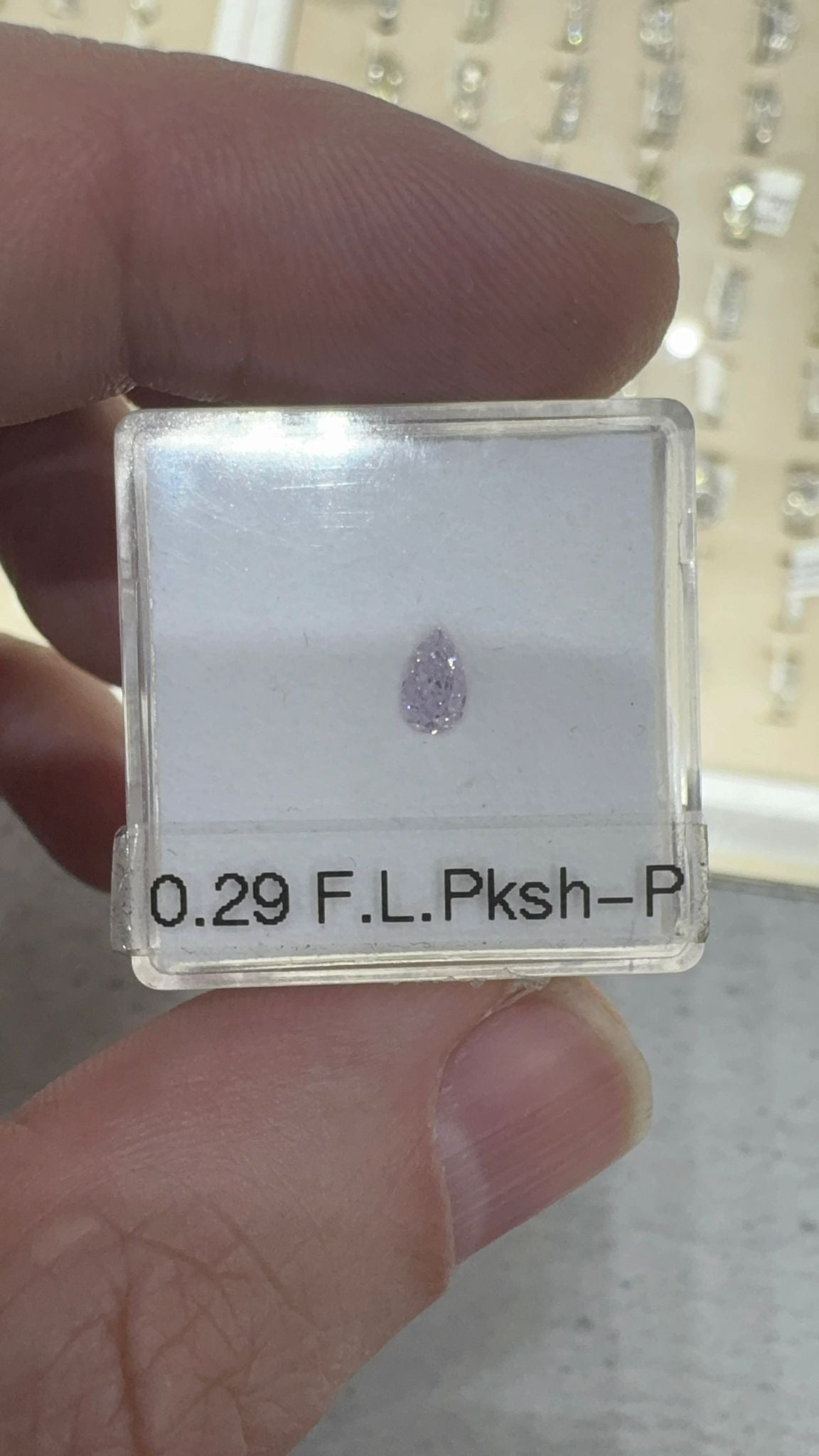 pear cut diamond in a clear holder with specifications on a hand