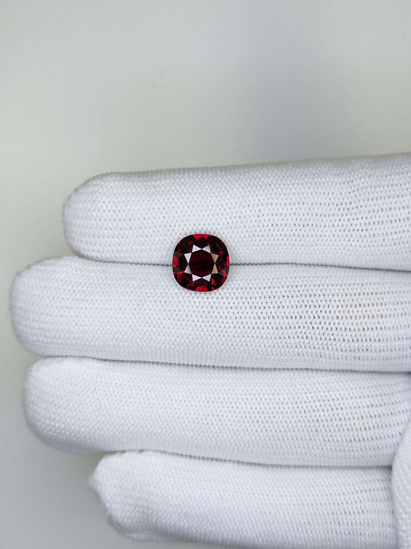 Cushion red ruby gemstone held between white gloves against a light gray background