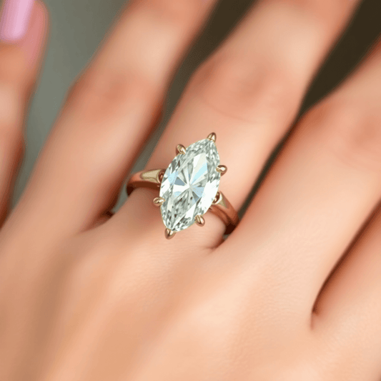 Close-up of a marquise-cut diamond ring in yellow gold, highlighting the diamond’s sparkle and elongated shape on an elegant blurred hand background.