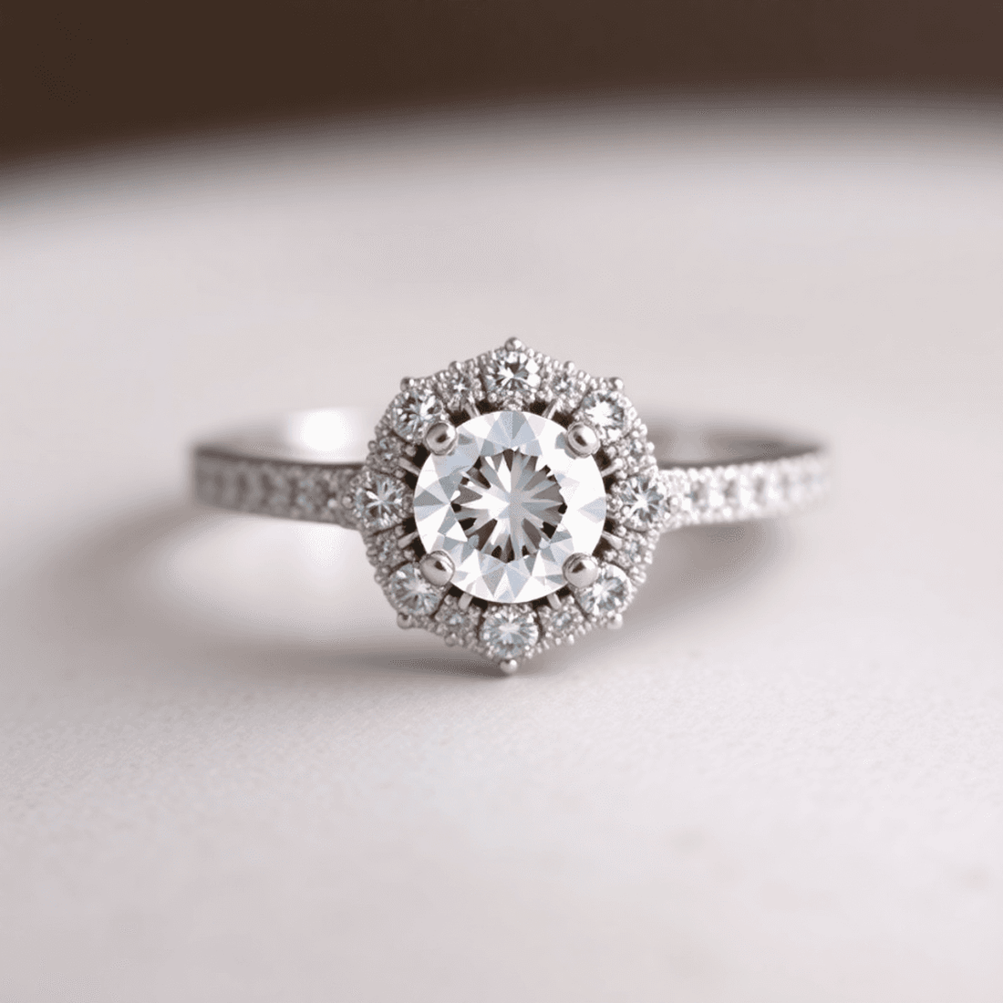 Close-up of a sparkling halo engagement ring with a large central diamond and smaller diamonds on an elegant band against a soft, blurred background.