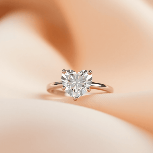 Close-up of a sparkling heart-shaped diamond ring on soft fabric, illuminated by warm light highlighting its brilliance and romantic design.