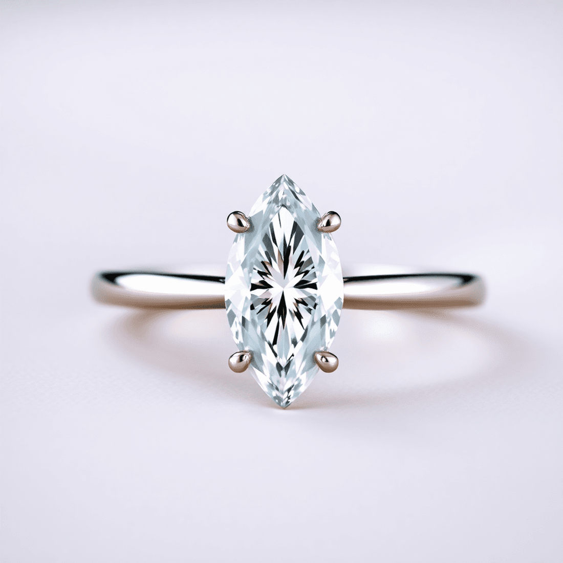 Close-up of a sparkling marquise cut diamond ring on a sleek metal band, displayed on a soft surface with subtle reflections and gentle lighting.