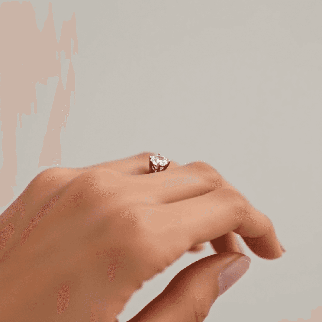Close-up of an elegant diamond ring with shared prong setting on a minimalist hand against a soft, neutral background.