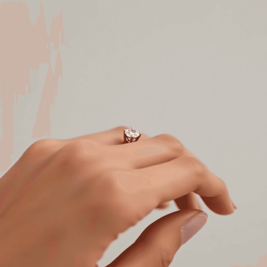 Close-up of an elegant diamond ring with shared prong setting on a minimalist hand against a soft, neutral background.