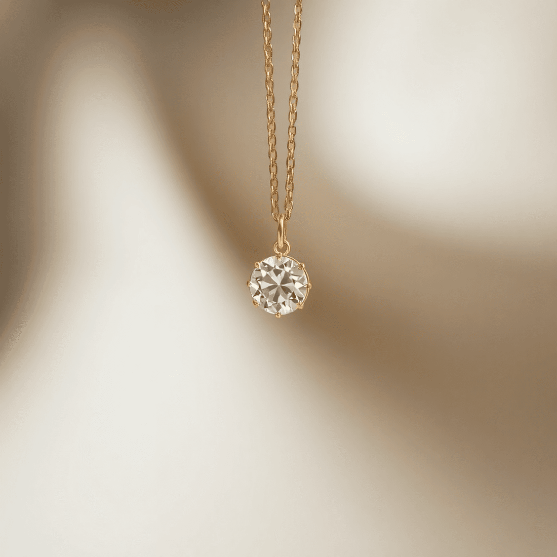 Close-up of a sparkling diamond pendant on a fine gold chain, softly lit to highlight its brilliance against a blurred neutral background.