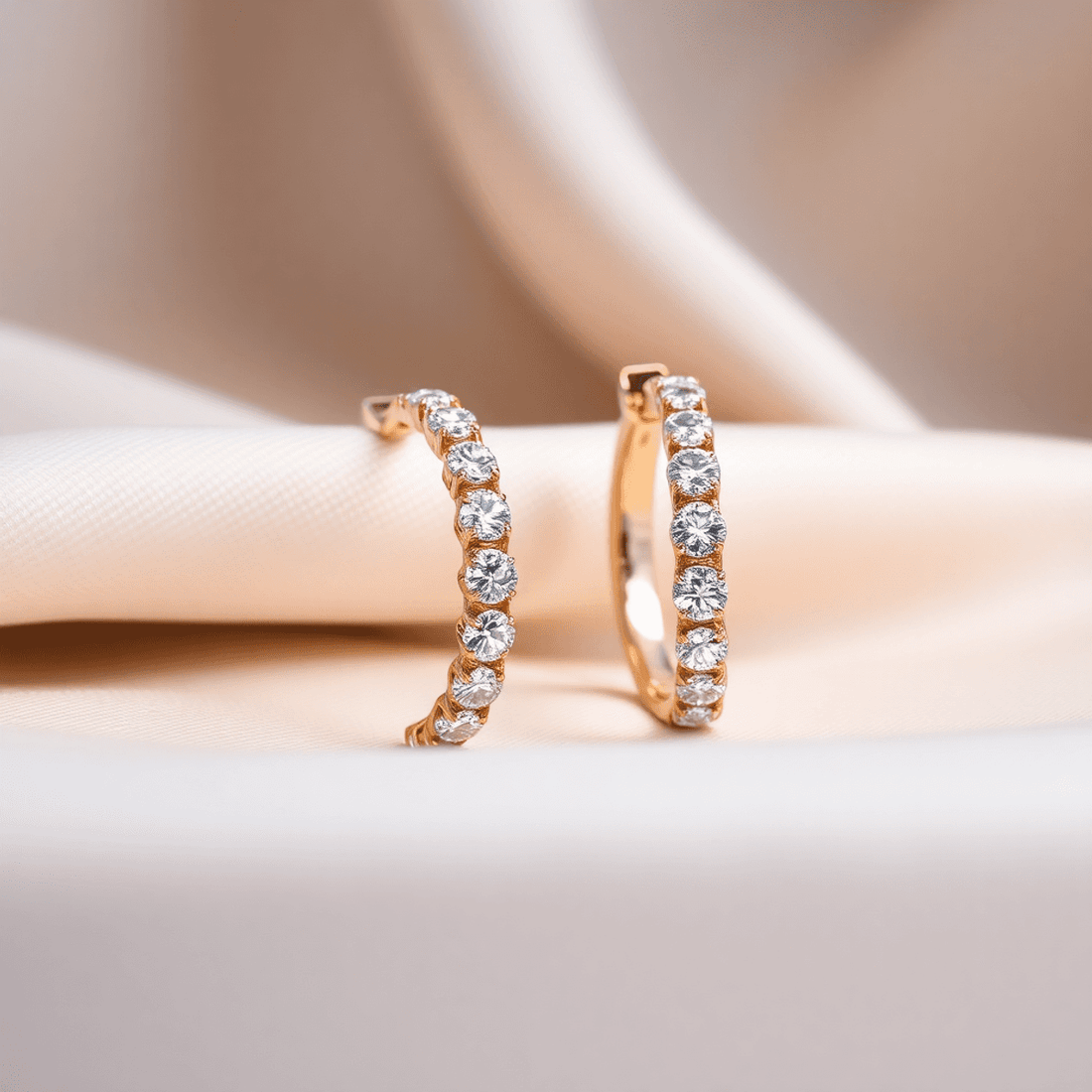 Close-up of sparkling diamond hoop earrings on soft fabric, highlighted by gentle lighting showcasing their brilliance and craftsmanship.