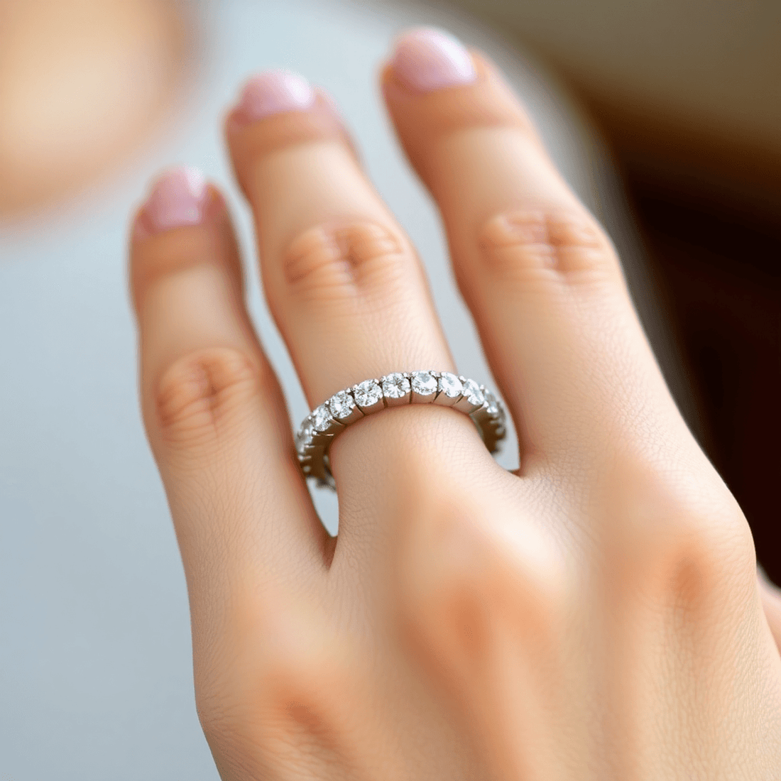 Close-up of a delicate diamond eternity ring on a manicured hand with soft blurred background and warm natural lighting.