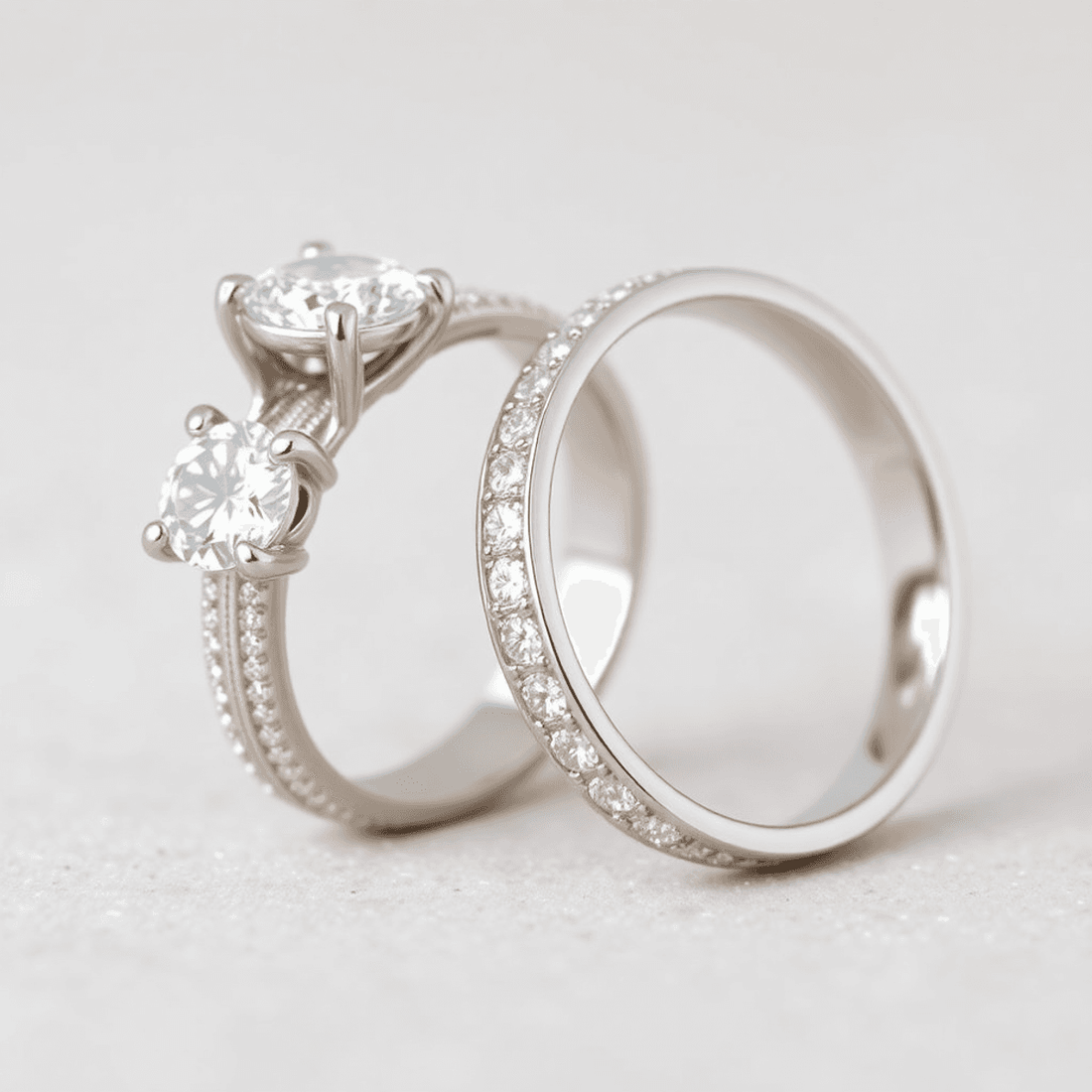 Close-up of two elegant white gold and platinum engagement rings on a soft neutral background, highlighting their shiny finishes and classic designs.