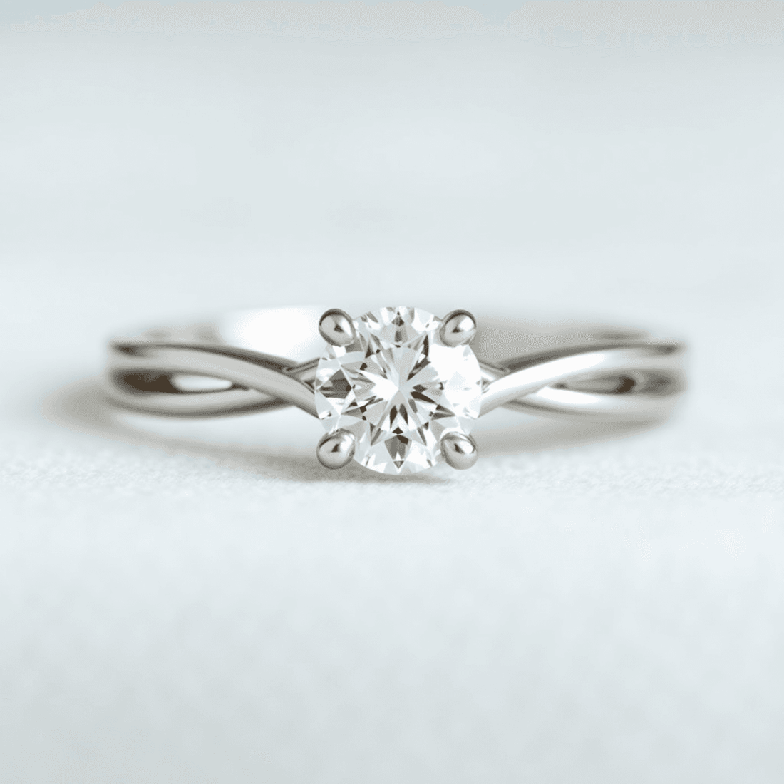 Close-up of an elegant split shank engagement ring with a sparkling center diamond on a soft, blurred background.