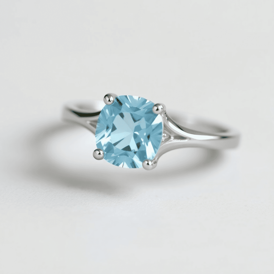 Close-up of an aquamarine engagement ring with a blue gemstone set in white gold, surrounded by small diamonds on a smooth neutral background.