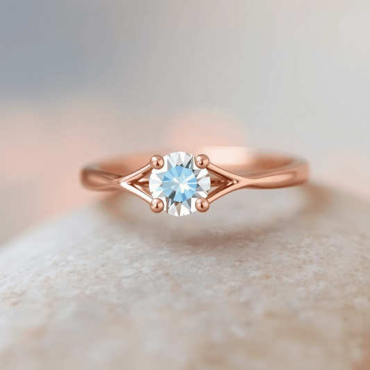 Close-up of a rose gold split shank ring with a sparkling center stone, highlighted by warm lighting and a soft, blurred background.