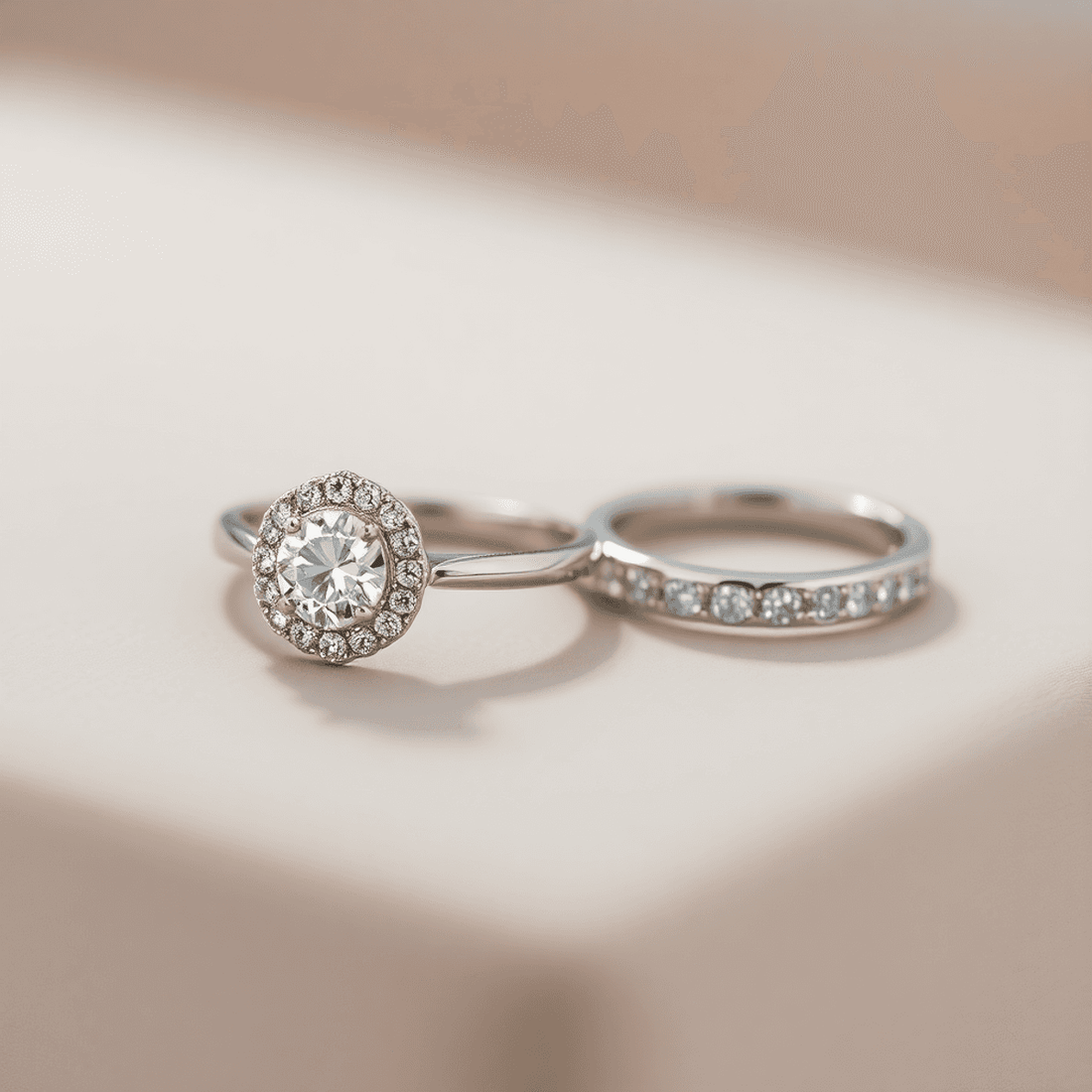 Close-up of a sparkling halo engagement ring and matching wedding band on a smooth surface, showcasing intricate details and delicate design under soft lighting