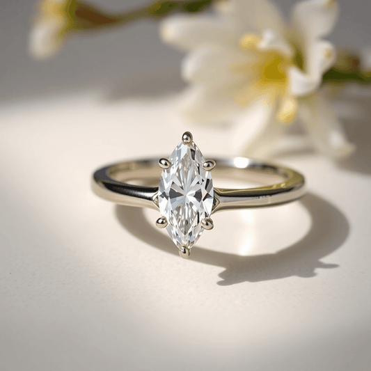 Close-up of a sparkling marquise cut diamond ring on an elegant band, highlighted by soft natural light with subtle floral accents on a neutral background.