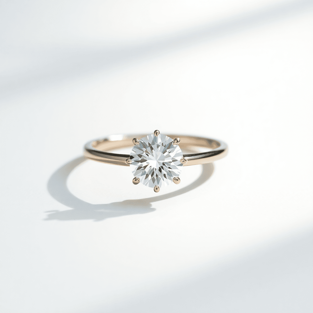 Close-up of a sparkling round brilliant diamond solitaire ring with a thin band on a neutral background, showcasing minimalist elegance and timeless beauty.