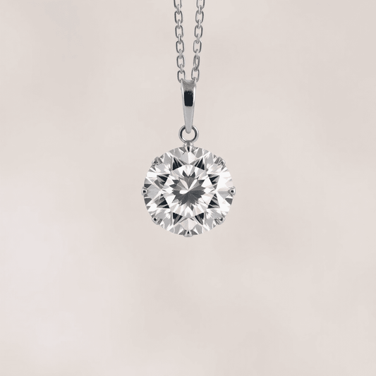 Close-up of a sparkling round brilliant diamond pendant on a delicate chain, glowing with radiant light reflections against a soft, blurred neutral background.