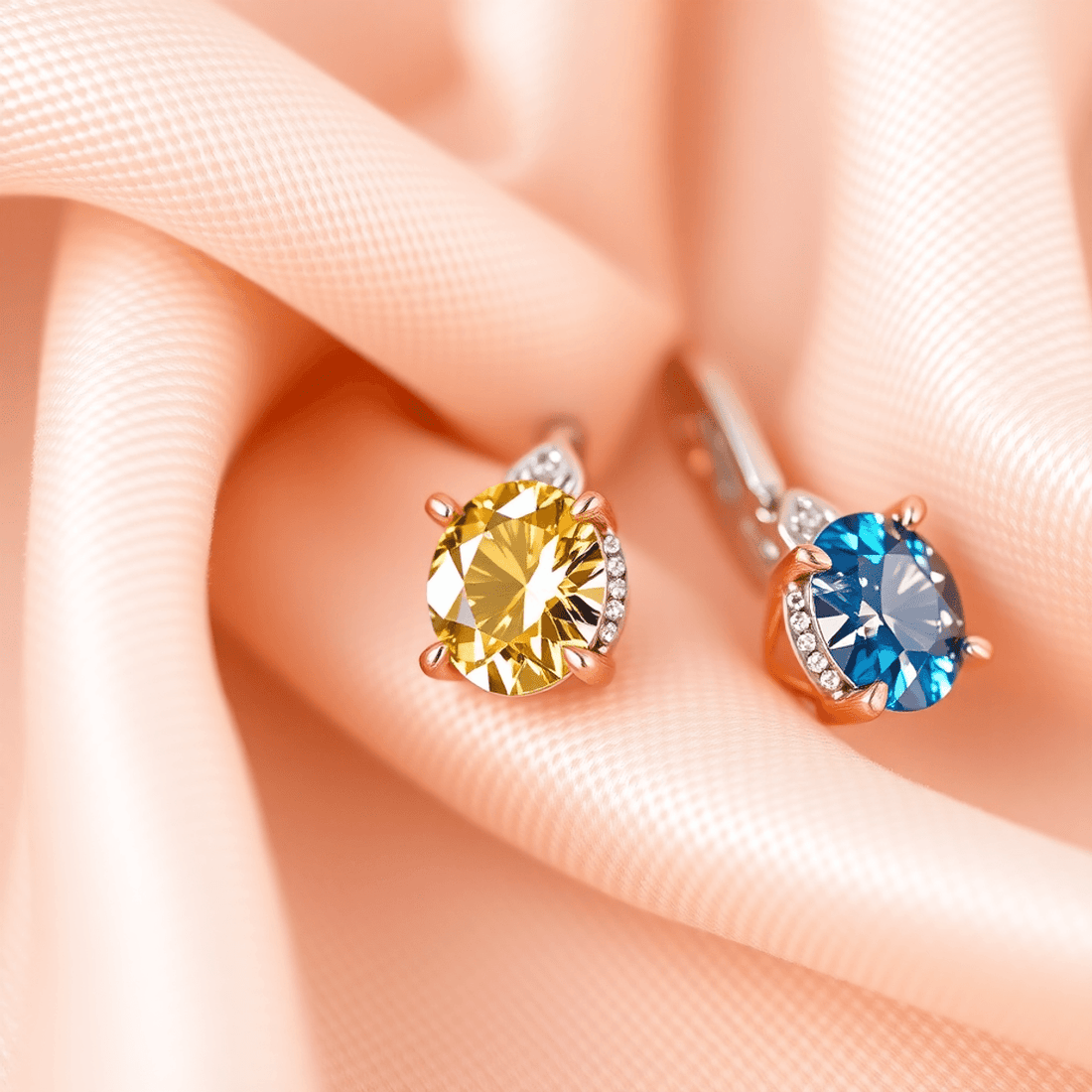 Close-up of sparkling colored diamond earrings in pink, yellow, and blue set in white and rose gold on soft fabric, highlighting luxury and fine craftsmanship.