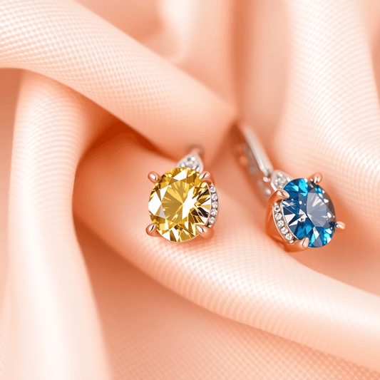 Close-up of sparkling colored diamond earrings in pink, yellow, and blue set in white and rose gold on soft fabric, highlighting luxury and fine craftsmanship.