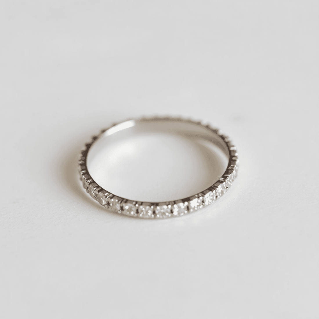 Close-up of an elegant eternity band ring with small sparkling diamonds on a softly lit neutral background.
