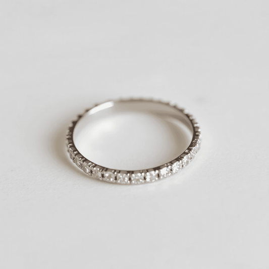 Close-up of an elegant eternity band ring with small sparkling diamonds on a softly lit neutral background.