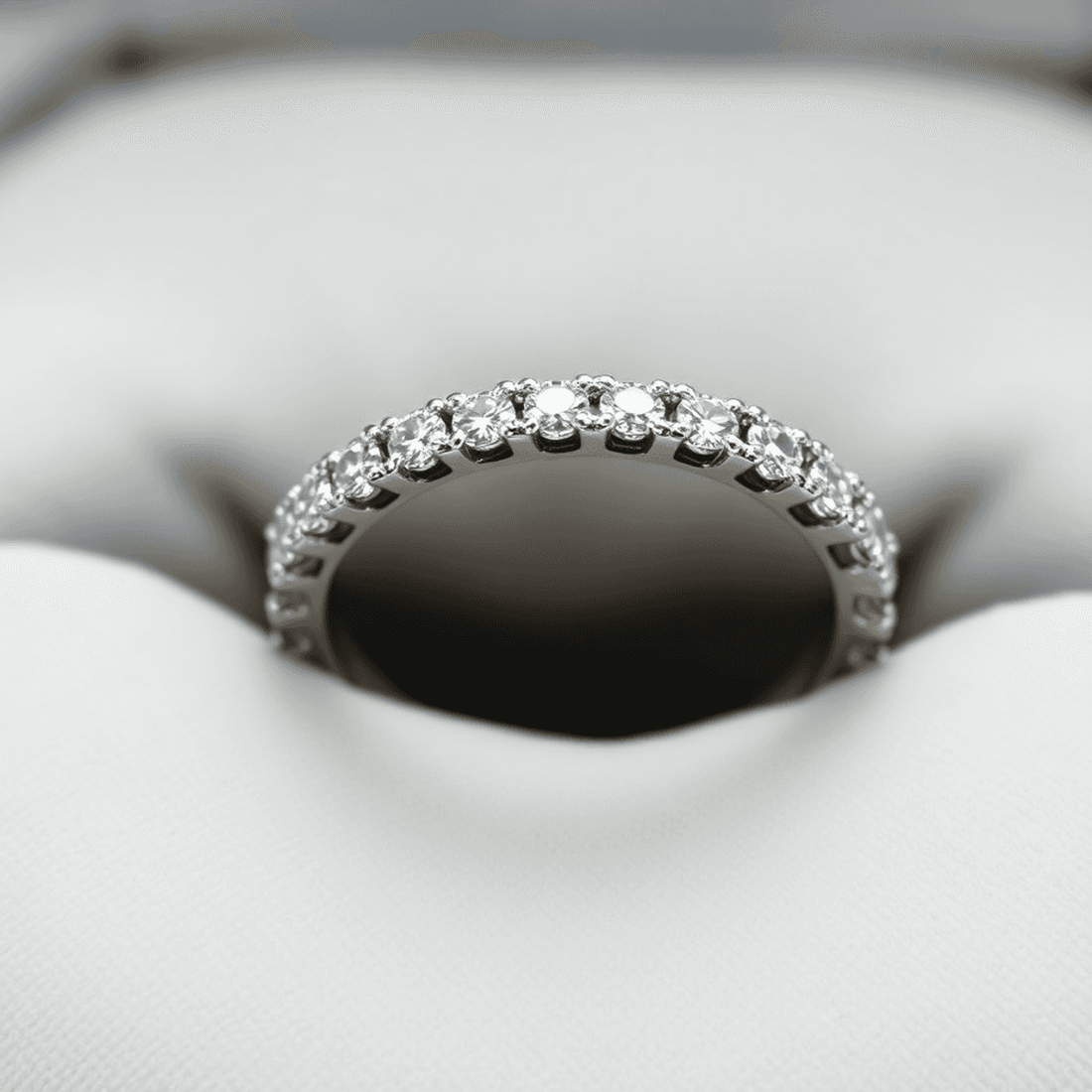 Close-up of a white gold diamond eternity wedding band on a soft velvet cushion, with gentle lighting highlighting the continuous circle of sparkling diamonds.