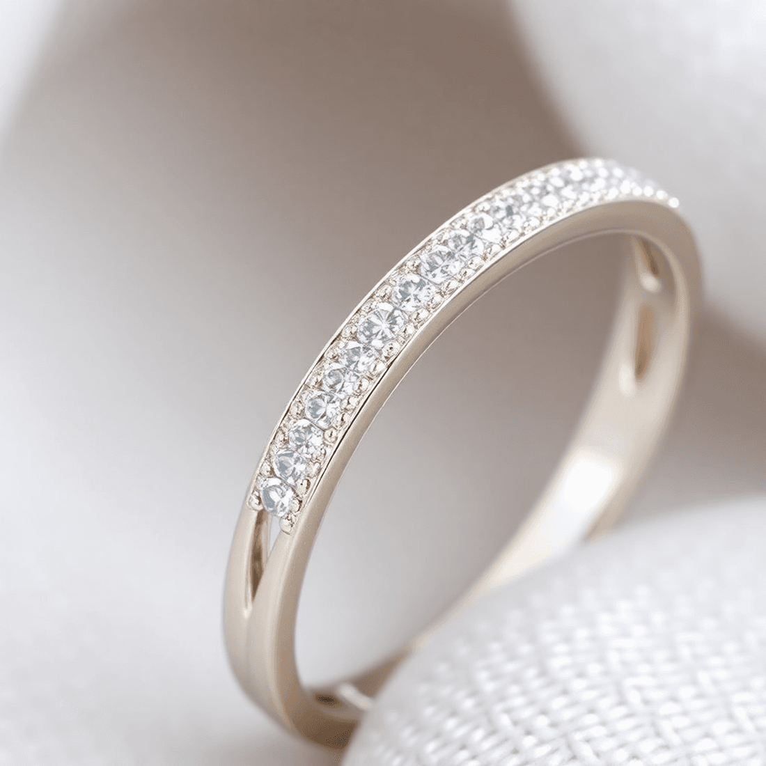 Close-up of an elegant split shank diamond ring with pavé-set diamonds on a sleek two-tone band against a soft, blurred background.