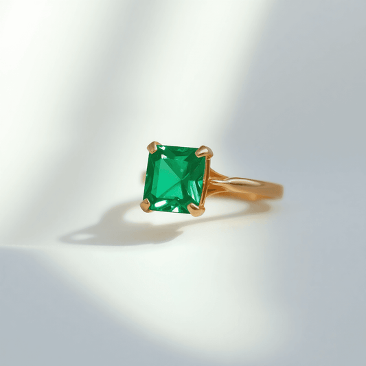Close-up of an emerald engagement ring with a vibrant green gemstone set in a gold band on a soft neutral background with natural light highlighting its depth.