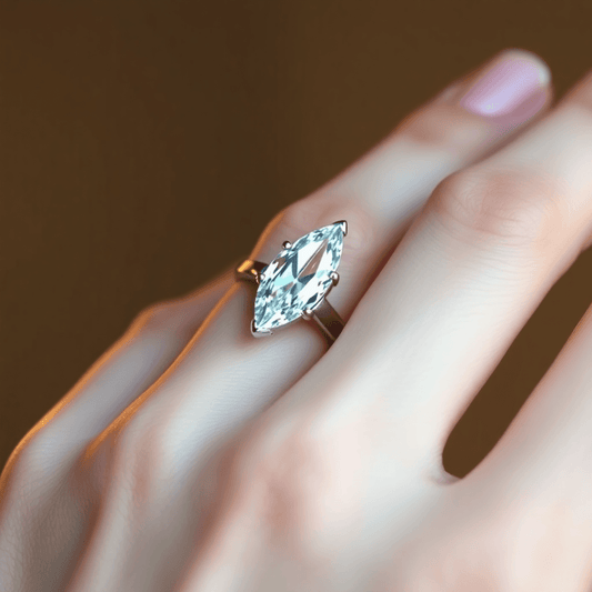 Close-up of a marquise cut diamond ring on a slender finger, with warm lighting highlighting the gemstone's brilliance against a blurred neutral background.