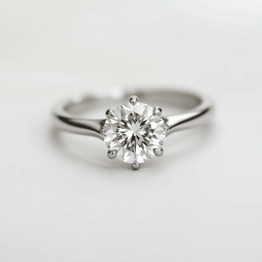Close-up of a sparkling round brilliant diamond ring in white gold or platinum on a soft, neutral background with light reflections highlighting its brilliance.