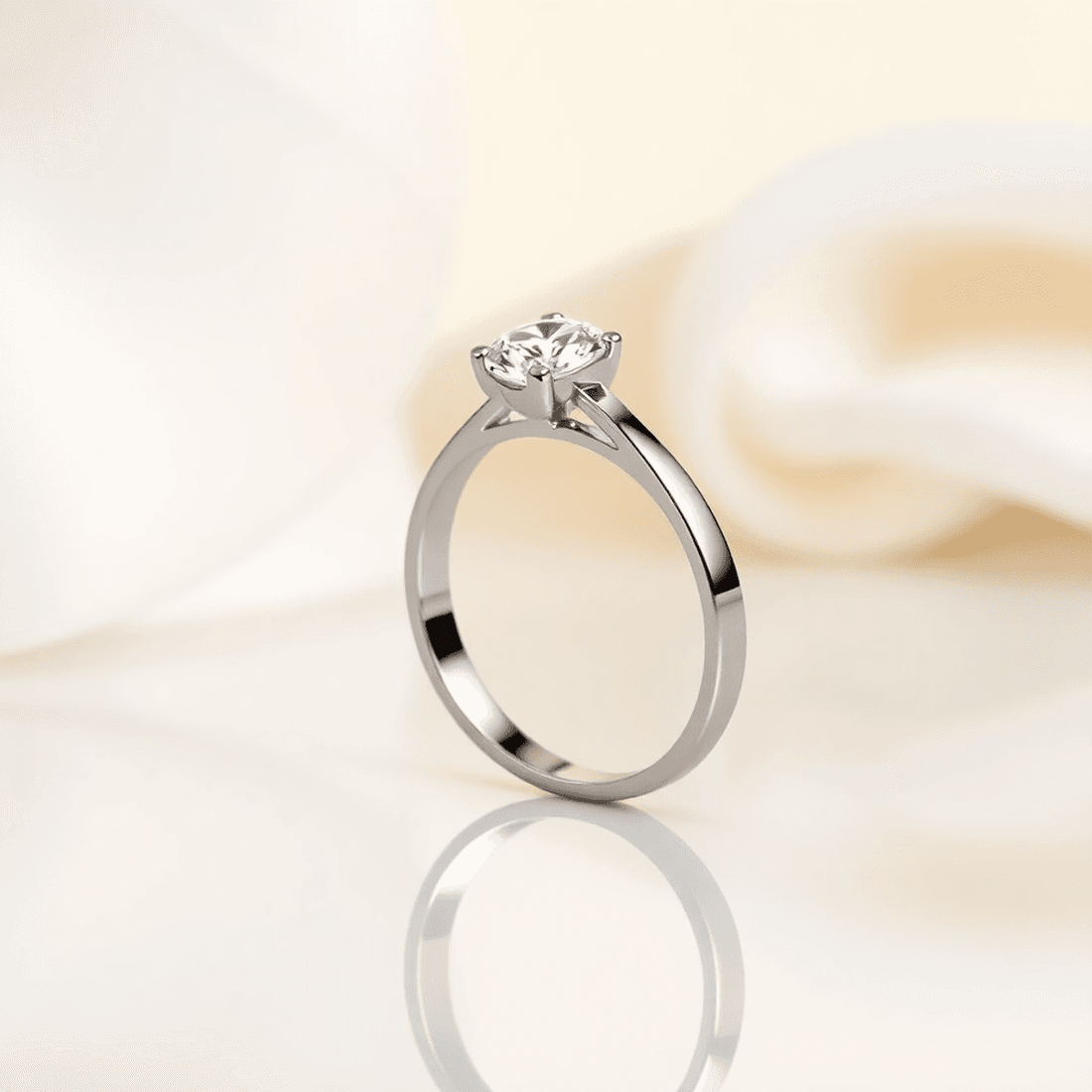 Close-up of a sleek engagement ring with a polished band and sparkling gemstone on a reflective surface with soft neutral background.