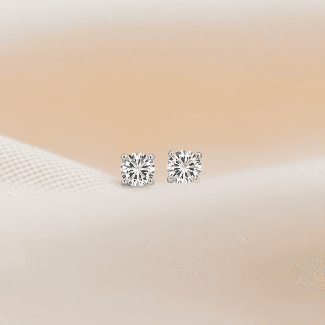 Close-up of elegant diamond stud earrings on soft neutral fabric, showcasing their sparkling simplicity and classic beauty in natural light.