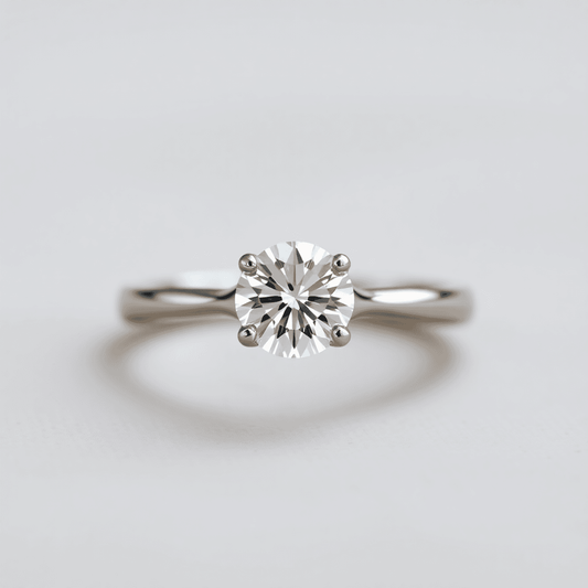 Close-up of a sparkling round brilliant diamond solitaire ring on a sleek platinum or gold band against a soft, neutral background with gentle lighting.