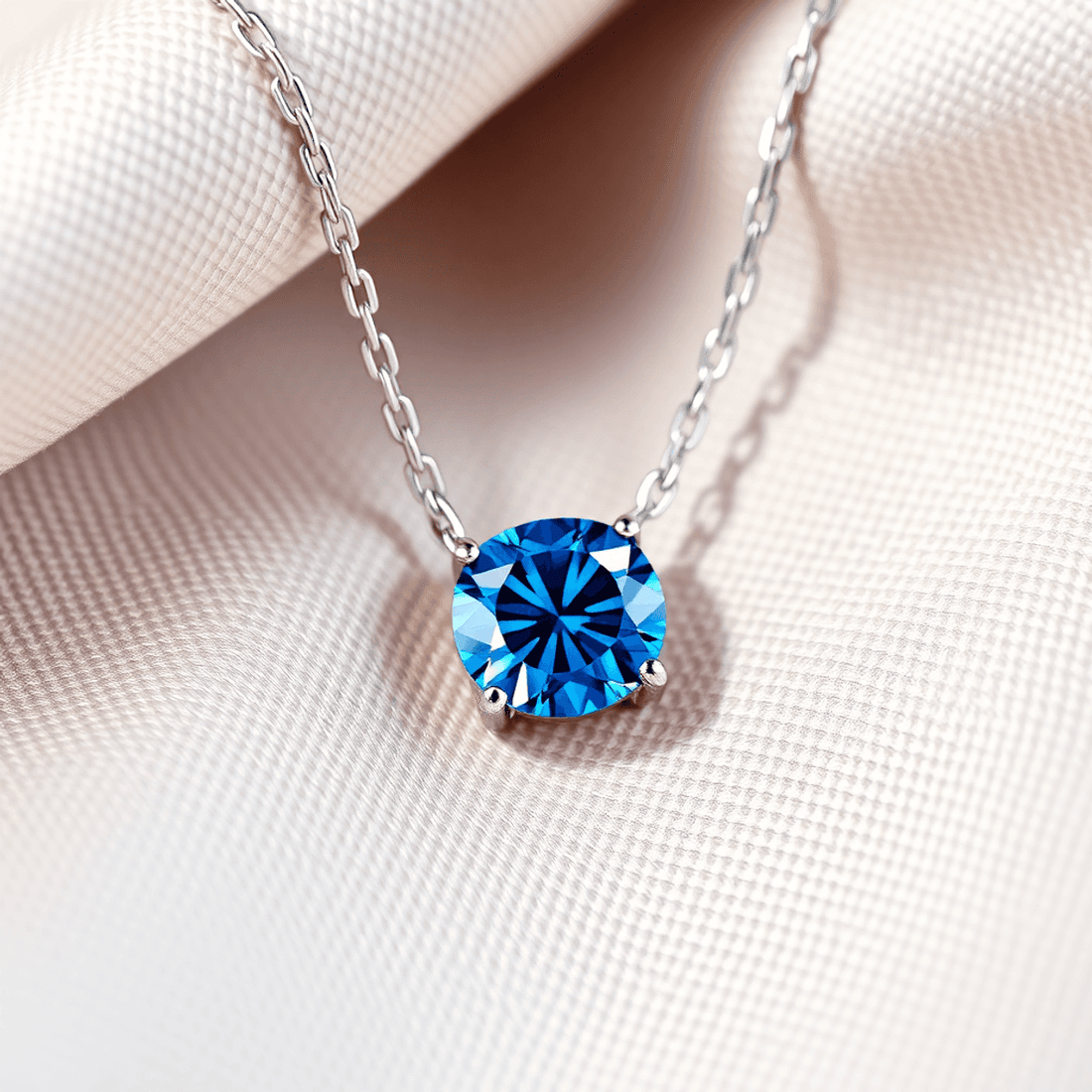 Close-up of a radiant blue diamond necklace on soft neutral fabric, with light reflections highlighting the deep blue hues and sparkling facets.