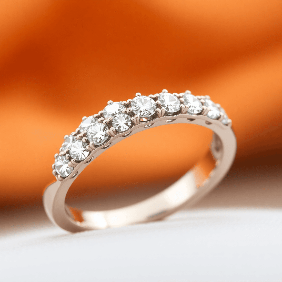 Close-up of a half eternity ring with sparkling diamonds on a polished metal band against a softly blurred warm background.