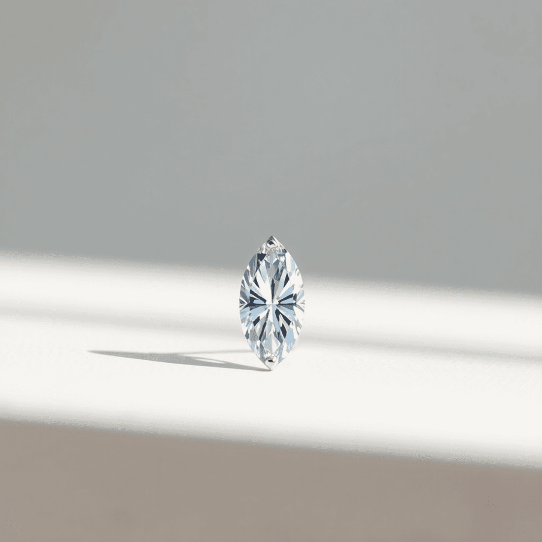 Close-up of a marquise cut diamond on a smooth surface with soft natural light highlighting its sparkling facets against a blurred neutral background.