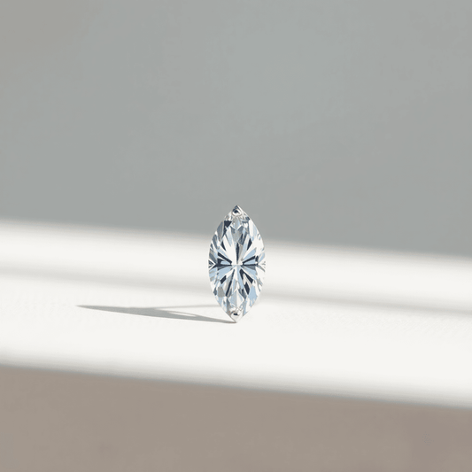 Close-up of a marquise cut diamond on a smooth surface with soft natural light highlighting its sparkling facets against a blurred neutral background.
