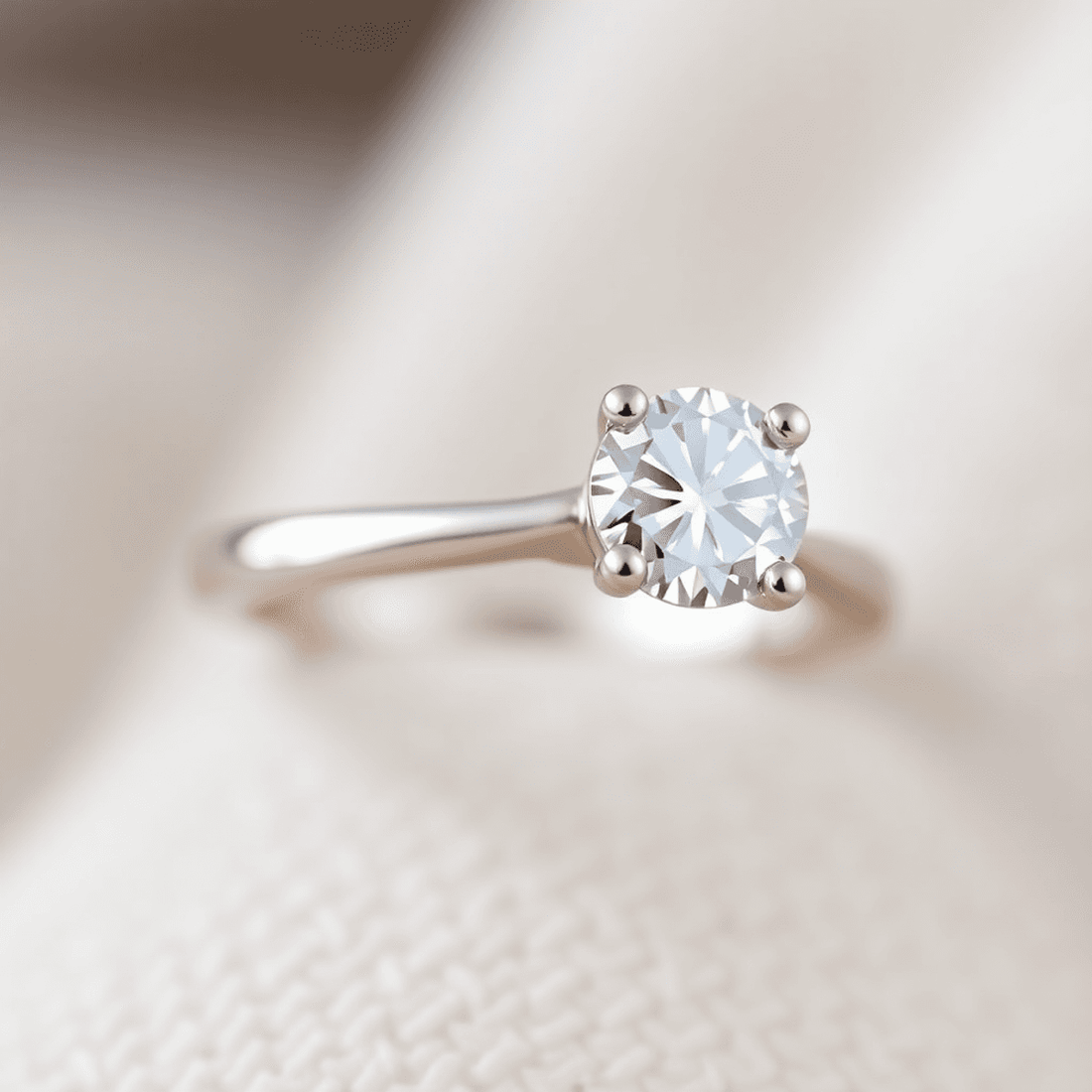 Close-up of a sparkling diamond engagement ring with slim shared prongs, glowing softly against a neutral blurred background.