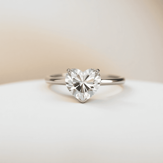 Close-up of a sparkling heart-shaped diamond ring on a soft neutral surface, with light reflections highlighting its brilliance and symmetry.