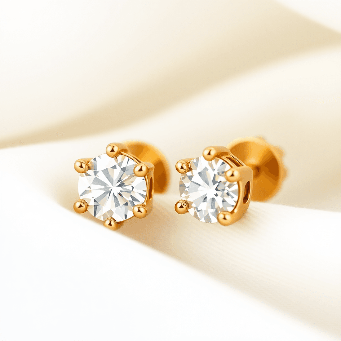 Close-up of sparkling diamond stud earrings in gold settings on soft white fabric, highlighting their brilliance and timeless elegance.