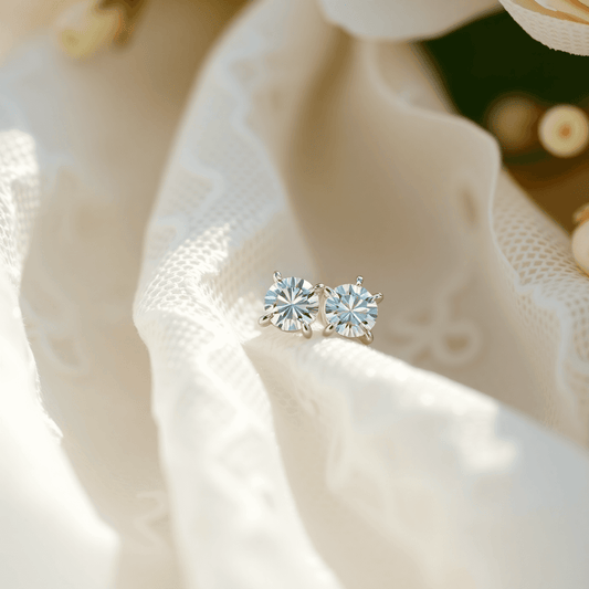 Close-up of sparkling diamond stud earrings on white lace fabric with soft flowers and gentle light, evoking bridal elegance and timeless sophistication.