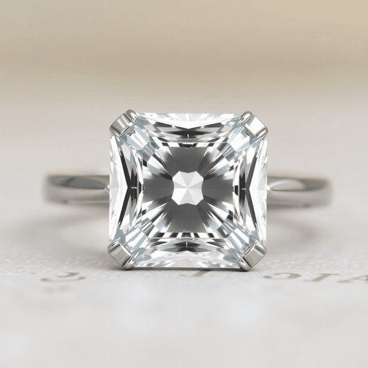 Close-up of a sparkling Asscher cut diamond ring with step-cut facets and cropped corners on a softly blurred neutral background.