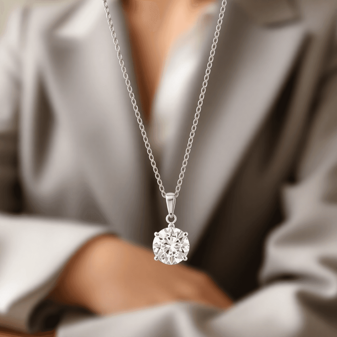 Close-up of a sparkling solitaire diamond pendant on a delicate white gold chain against a soft, neutral background with blurred professional attire.