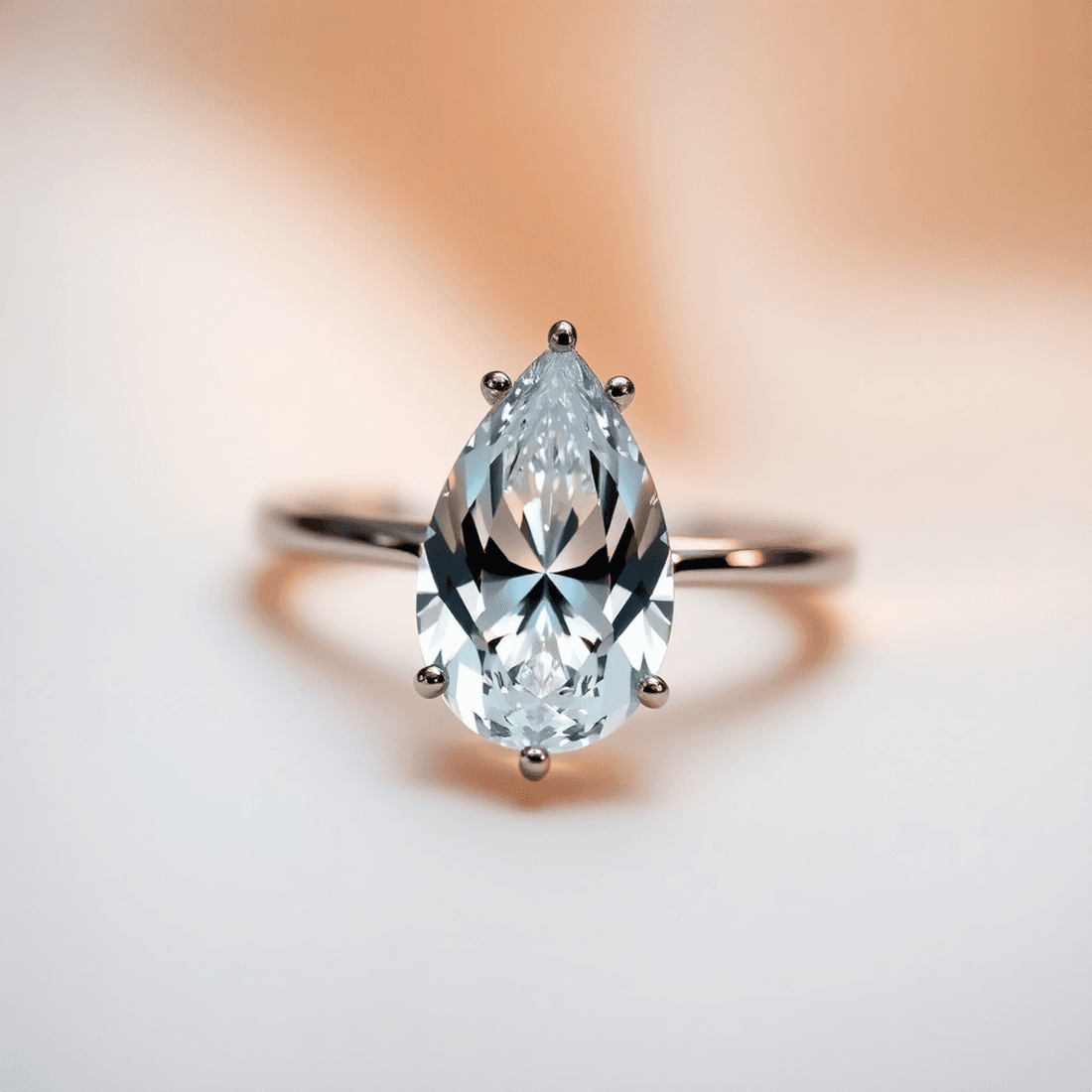 Close-up of a sparkling pear-shaped diamond ring on a soft, blurred background with gentle light reflections highlighting its teardrop shape.