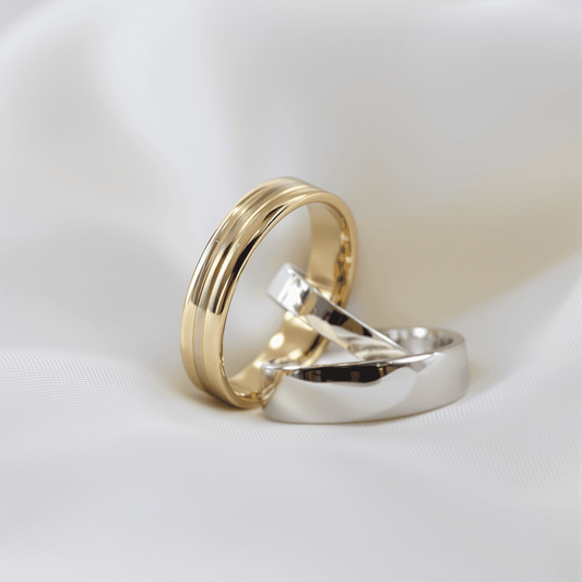 Close-up of two wedding bands, one yellow gold and one platinum, resting on soft white fabric.