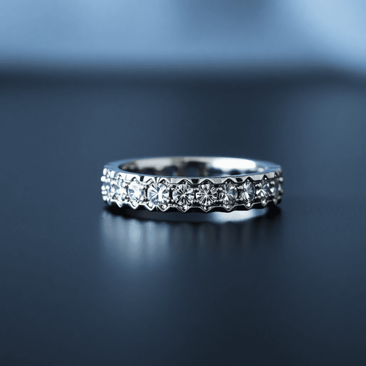 Close-up of a men's diamond eternity band on a dark surface, showcasing sparkling diamonds in a polished metal band with a softly blurred background.