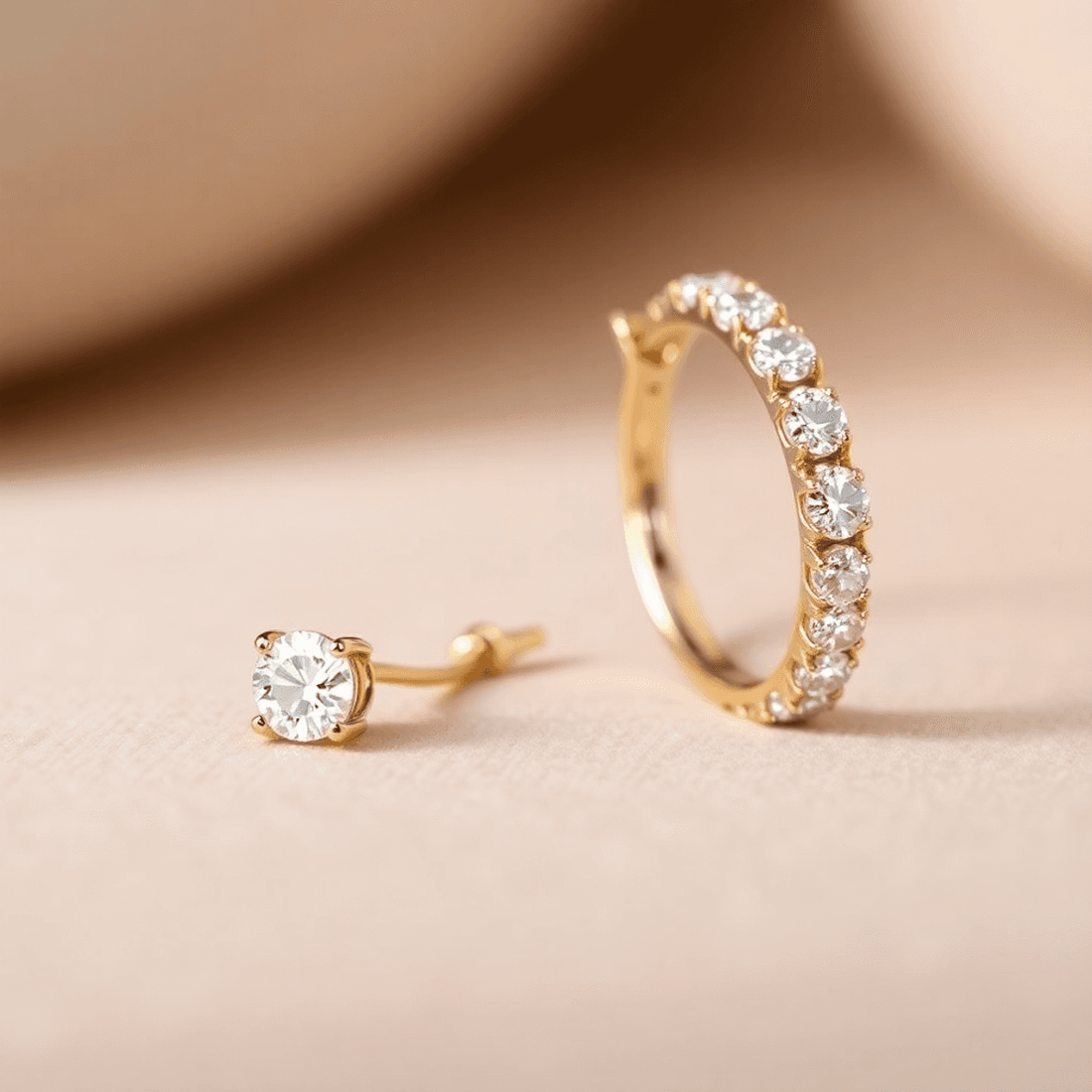 Close-up of two pairs of diamond hoop earrings, small and large, on a soft neutral background with sparkling stones and gold settings.