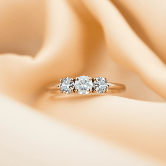 Close-up of a three-stone engagement ring with sparkling gems on a soft fabric, highlighted by warm natural lighting.