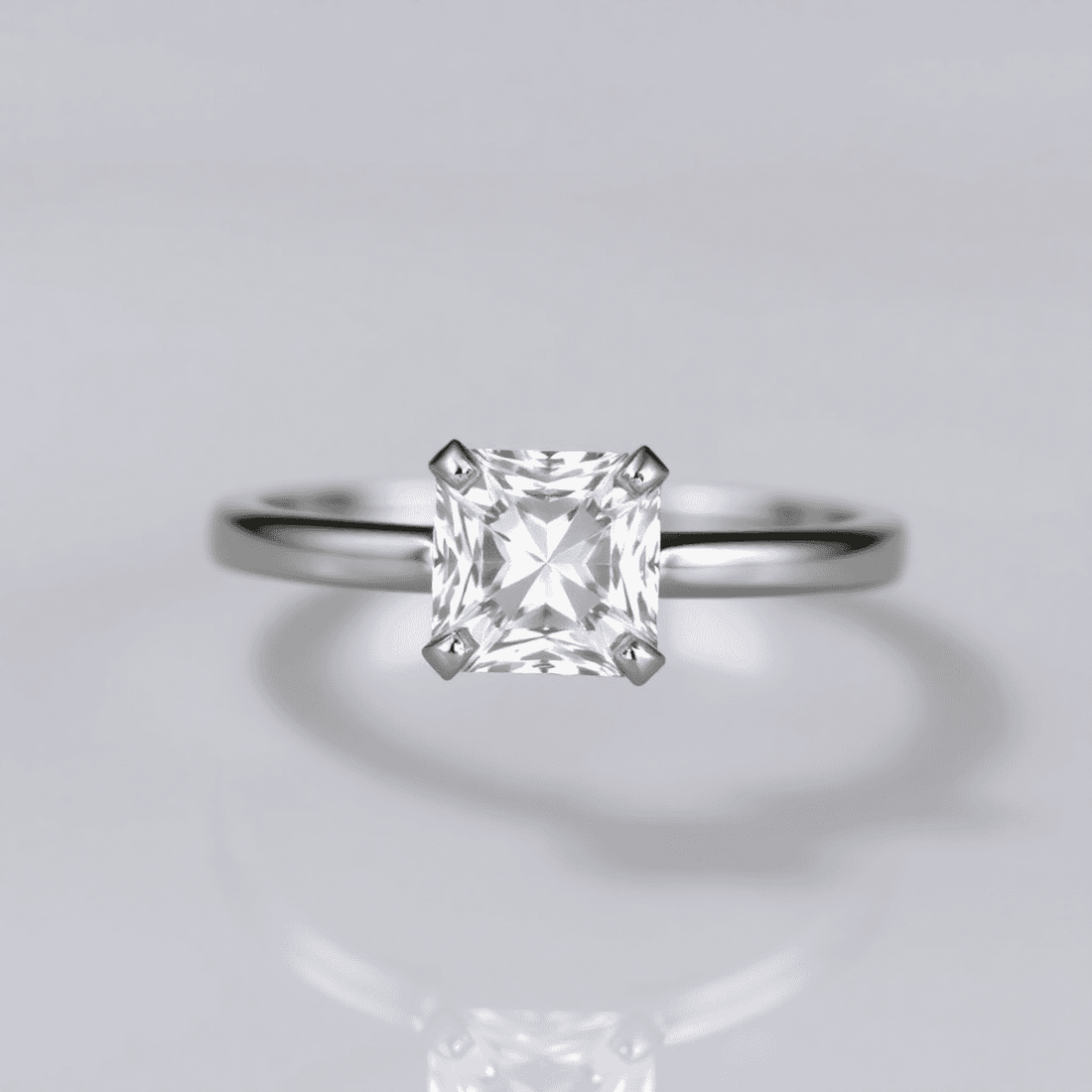 Close-up of a sparkling Asscher cut diamond ring on a sleek metal band, shown on a soft background with reflections highlighting its geometric facets.