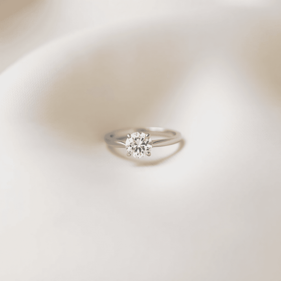Close-up of a sparkling solitaire diamond ring with a simple band on a soft, neutral background, highlighting minimalism and timeless elegance.