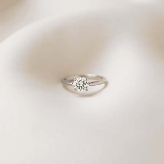 Close-up of a sparkling solitaire diamond ring with a simple band on a soft, neutral background, highlighting minimalism and timeless elegance.