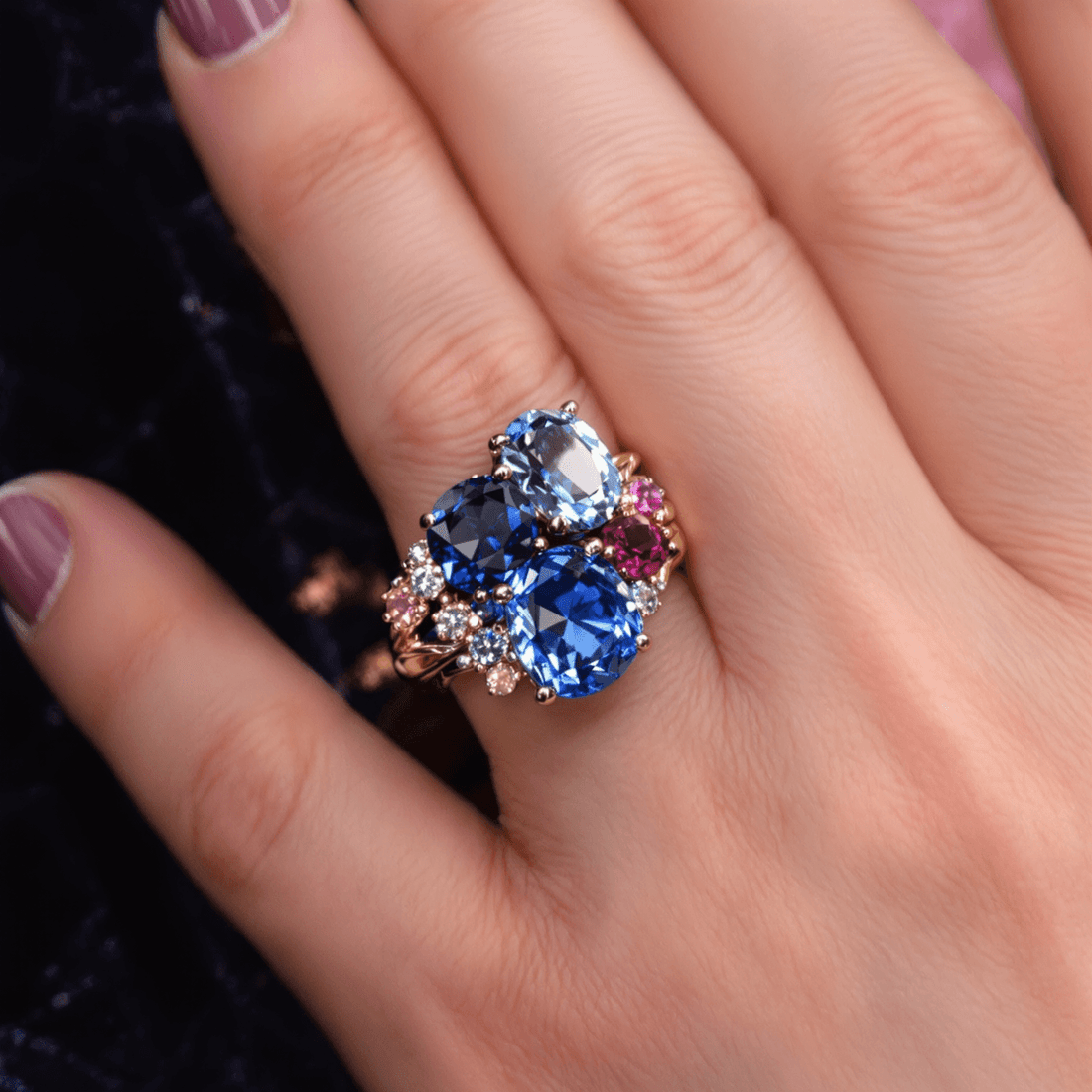 Close-up of a gold sapphire ring with blue and pink sapphires and diamonds on dark velvet, highlighting the gems' brilliance and intricate craftsmanship.